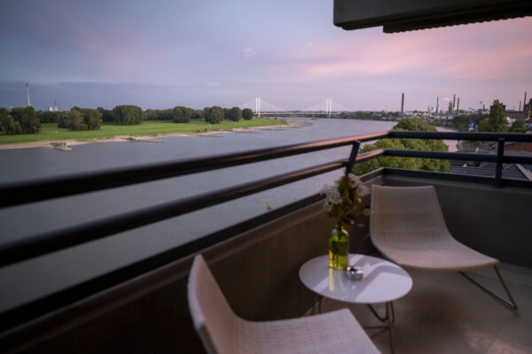 Balkon mit Sitzgelegenheiten und Tisch im Hotel Rheingarten mit Blick auf den Fluss und die Brücke bei Sonnenuntergang