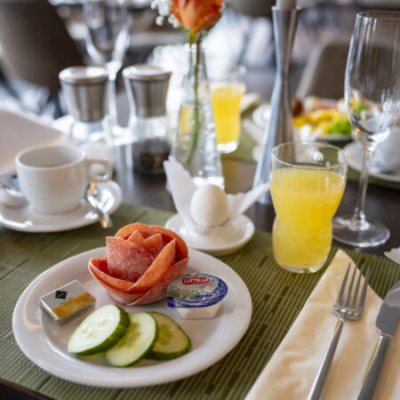 Frühstücksteller im Hotel Rheingarten mit Wurst, Gurkenscheiben, Butter, Käse, Ei und Orangensaft