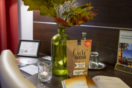 Dekorierter Schreibtisch im Hotelzimmer mit Vase, Kerze, Getränken und einem Buch im Hotel Rheingarten