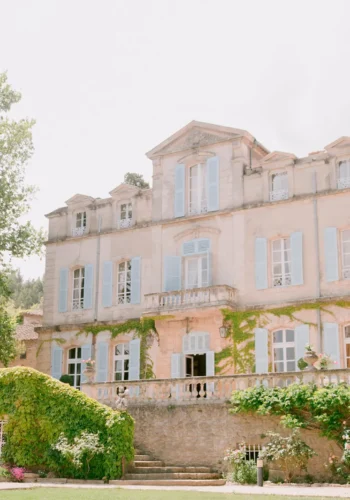 Charmantes französisches Landhaus mit hellblauen Fensterläden, umgeben von grünen Bäumen und einer sonnigen Gartenterrasse, ideal für Hochzeiten oder romantische Aufenthalte