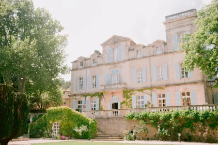 Charmantes französisches Landhaus mit hellblauen Fensterläden, umgeben von grünen Bäumen und einer sonnigen Gartenterrasse, ideal für Hochzeiten oder romantische Aufenthalte