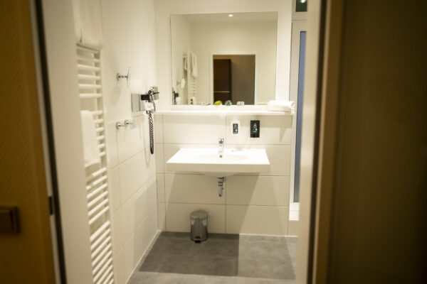 Modernes, helles Badezimmer im Hotel Rheingarten mit großem Spiegel, Waschbecken und Handtuchhalter.