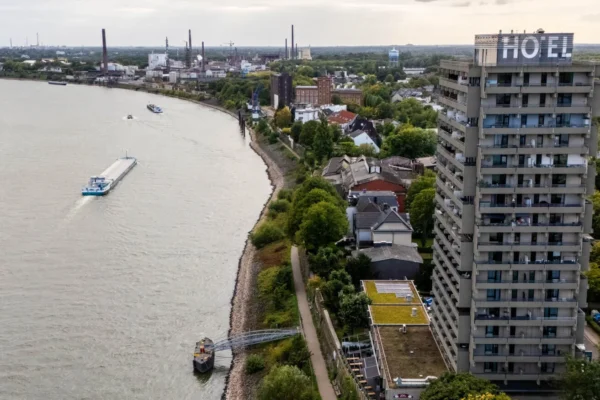 Drohnenaufnahme des Hotel Rheingarten in Duisburg mit Blick auf den Rhein, vorbeifahrende Schiffe und die umliegende Landschaft.