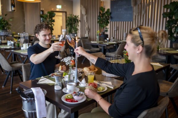 Gäste genießen ein Frühstück im Restaurant des Hotel Rheingarten und stoßen mit einem Glas Sekt an, umgeben von gemütlicher Atmosphäre und stilvoller Einrichtung.