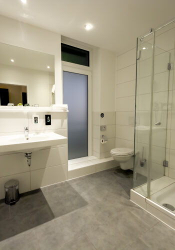 Modernes Badezimmer im Hotel Rheingarten mit großer Glasdusche, Waschbecken und WC.