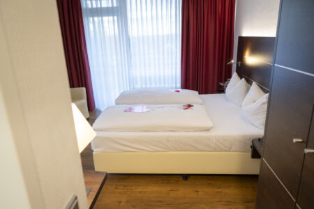 Gemütliches Hotelzimmer im Hotel Rheingarten mit Doppelbett, roter Fensterdekoration und liebevoller Bettdekoration in Herzform.