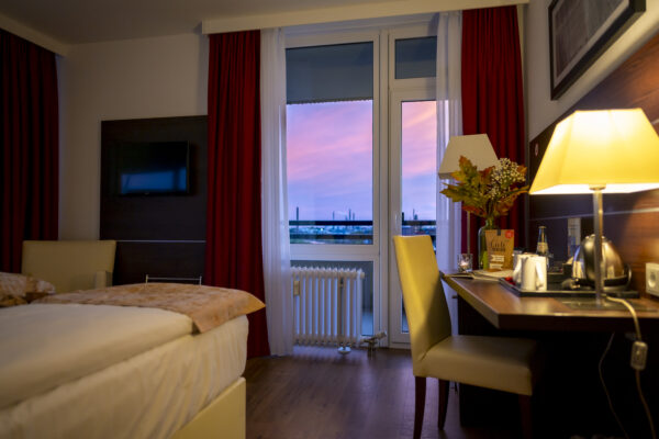 Modernes Hotelzimmer im Hotel Rheingarten mit Schreibtisch, warmem Licht und Blick auf den Rhein bei Sonnenuntergang.