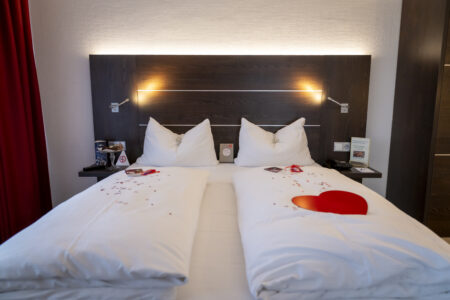 Romantisch dekoriertes Doppelzimmer im Hotel Rheingarten mit Herzdekoration und Rosenblättern auf dem Bett.