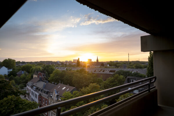 Aussicht vom Balkon des Hotel Rheingarten in Duisburg bei Sonnenuntergang mit Blick über die Stadt, Bäume und Kirchturm.