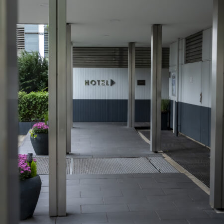 Eingangsbereich des Hotel Rheingarten in Duisburg mit überdachtem Zugang, modernen Säulen und Blumendekoration.