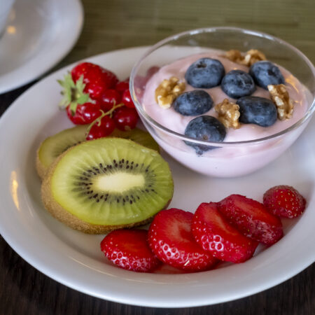 Frühstücksteller im Hotel Rheingarten in Duisburg mit Kiwi, Erdbeeren, Johannisbeeren und einer Schale Joghurt mit Blaubeeren und Walnüssen.