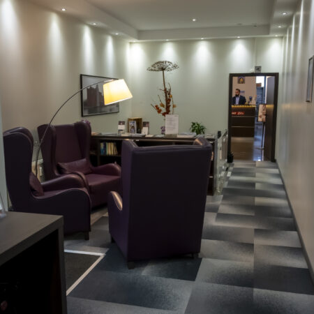 Gemütlicher Sitzbereich im Hotel Rheingarten in Duisburg mit bequemen Sesseln, Lesematerialien, Stehlampe und Blick zur Rezeption.