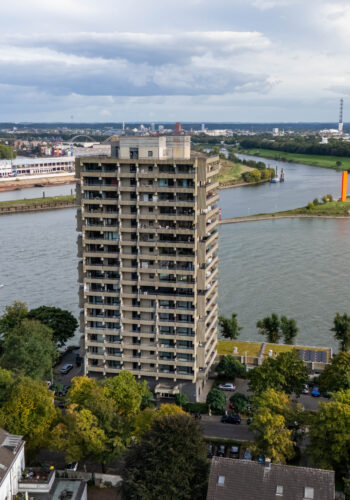 Luftaufnahme des Hotel Rheingarten in Duisburg direkt am Rhein mit Blick auf den Fluss, die Uferwiesen und die markante orangefarbene Skulptur.