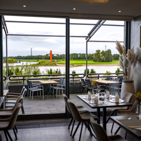 Restaurant im Hotel Rheingarten in Duisburg mit gedeckten Tischen und großem Panoramafenster, Blick auf den Rhein und die Uferwiesen.