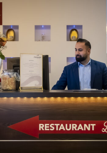Rezeption im Hotel Rheingarten in Duisburg mit freundlichem Mitarbeiter am Empfangstresen, Dekoration und Hinweis zum Restaurant LuMar.