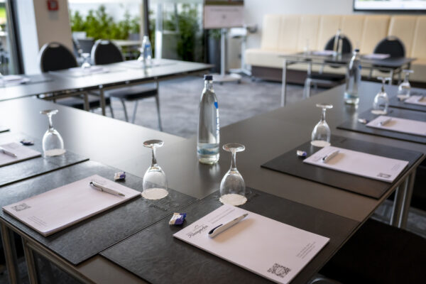 Detailaufnahme eines Konferenztisches im Hotel Rheingarten in Duisburg, vorbereitet mit Schreibunterlagen, Stiften, Gläsern und Mineralwasser für eine Tagung.