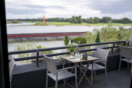 Terrassentisch des Hotel Rheingarten in Duisburg mit Sitzgelegenheiten direkt am Rhein und Blick auf die Uferwiesen.