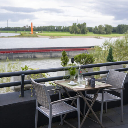 Terrassentisch des Hotel Rheingarten in Duisburg mit Sitzgelegenheiten direkt am Rhein und Blick auf die Uferwiesen.