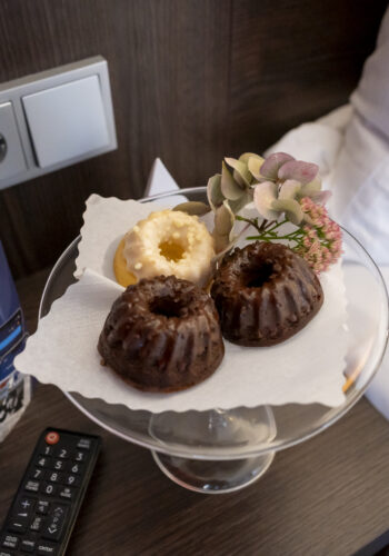 Kleine Gugelhupf-Kuchen und Gebäck als Willkommensgruß im Hotel Rheingarten in Duisburg, serviert auf einem Glasteller mit Blume.