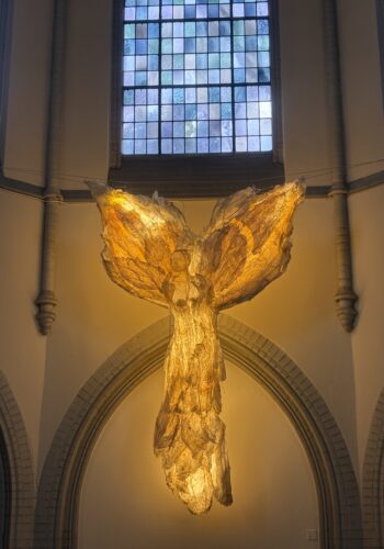 Leuchtende Engel-Installation im Kolumbarium Duisburg vor einem großen Kirchenfenster.