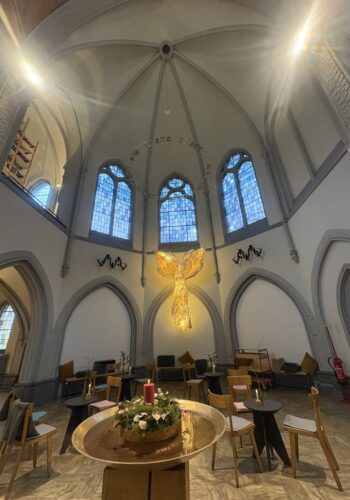 Begegnungsraum im Kolumbarium Duisburg mit hohen Kirchenfenstern und leuchtender Engel-Installation.