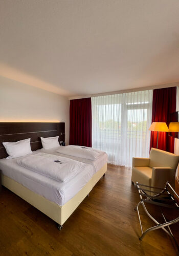 Hotelzimmer mit Doppelbett, Sessel, Holzboden und Balkonzugang