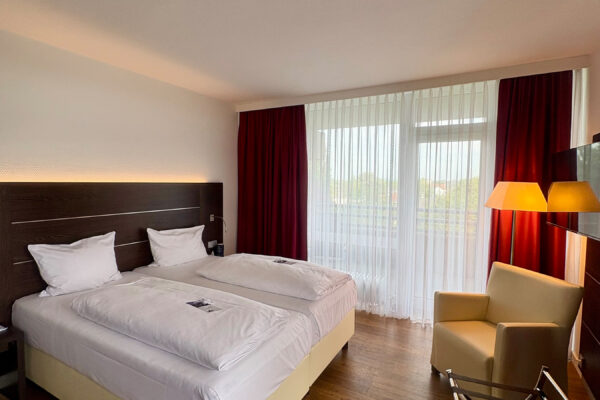 Hotelzimmer mit Doppelbett, Sessel, Holzboden und Balkonzugang