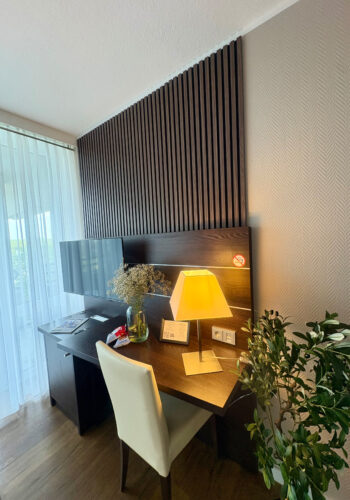 Schreibtischbereich im Hotelzimmer mit Holzverkleidung, Lampe und Fernseher