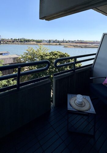Überdachter Balkon mit dunklem Loungesessel, kleinem Tisch und Panoramablick über das Wasser