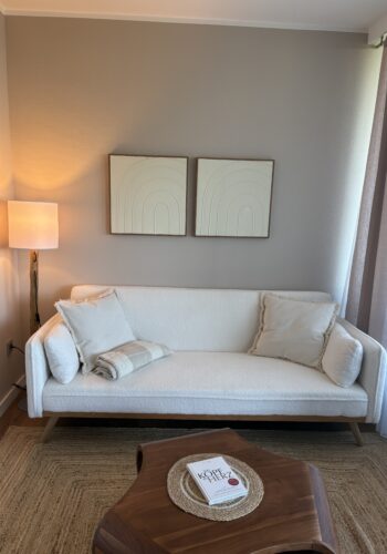 Frontaler Blick auf einen hellen Sitzbereich mit weißem Sofa, Stehlampe und Holztisch