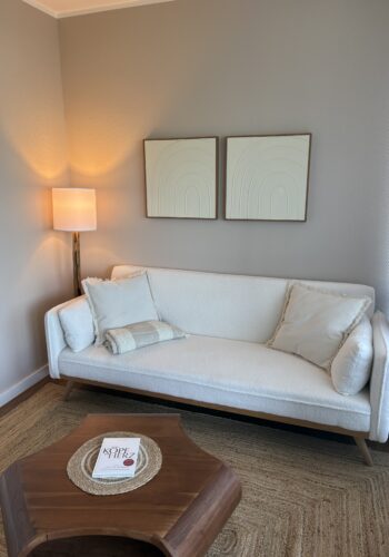 Heller Sitzbereich mit weißem Sofa, Stehlampe, Wandbildern und kleinem Holztisch