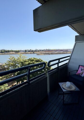 Überdachter Balkon mit dunkler Lounge-Sitzecke, pinkfarbenen Kissen und weitem Wasserblick